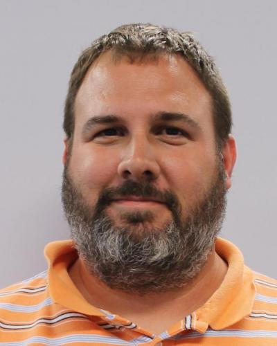 A man with short hair and a beard wearing an orange polo shirt.